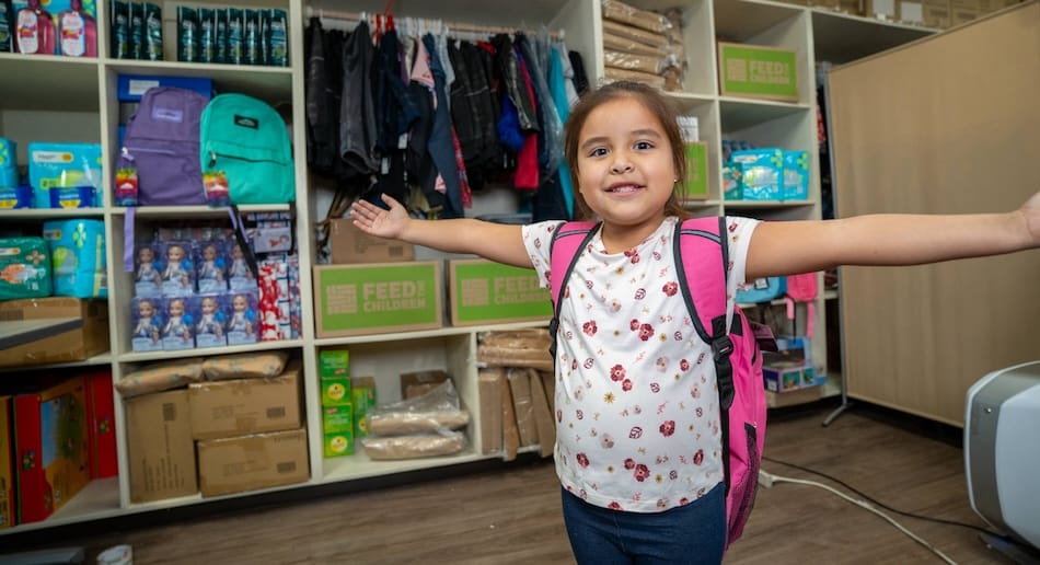 Un niño extendiendo los brazos delante de material escolar